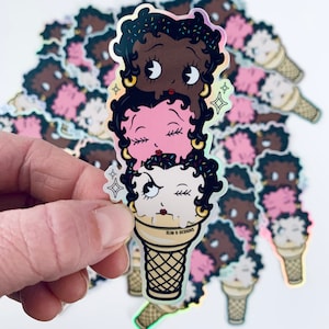 May include: A sticker of three cartoon faces stacked on top of each other in an ice cream cone. The faces are black, pink, and white with closed eyes and eyelashes. The cone is brown and white with the text "SLIM & DESIGNS" printed on the side.