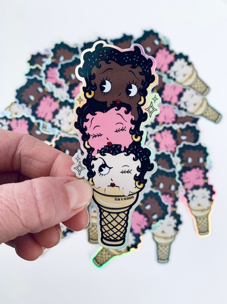 May include: A sticker of three cartoon faces stacked on top of each other in an ice cream cone. The faces are black, pink, and white with closed eyes and eyelashes. The cone is brown and white with the text "SLIM & DESIGNS" printed on the side.