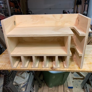May include: A wooden storage shelf with multiple compartments and a shelf on top. The shelf is made of light-colored wood and has a simple design.