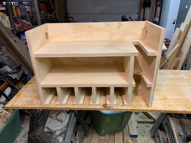 May include: A wooden storage shelf with multiple compartments and a shelf on top. The shelf is made of light-colored wood and has a simple design.