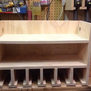 May include: A wooden shelf unit with two shelves and multiple compartments below. The shelf unit is made of light-colored wood and has a simple design.
