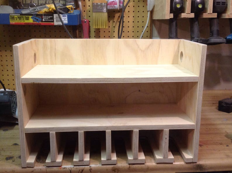 May include: A wooden shelf unit with two shelves and multiple compartments below. The shelf unit is made of light-colored wood and has a simple design.