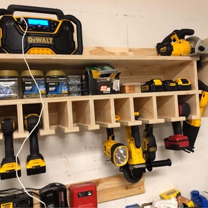 May include: A wooden wall-mounted storage rack with multiple compartments for organizing tools. The rack features a yellow and black DeWalt radio, several jars of screws, and various yellow and black power tools, including drills, a circular saw, and a grinder.