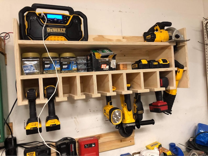 May include: A wooden wall-mounted storage rack with multiple compartments for organizing tools. The rack features a yellow and black DeWalt radio, several jars of screws, and various yellow and black power tools, including drills, a circular saw, and a grinder.