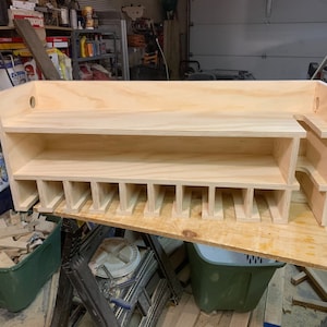 May include: A wooden shelf unit with multiple compartments for storage. The shelf is made of unfinished plywood and has a simple design.