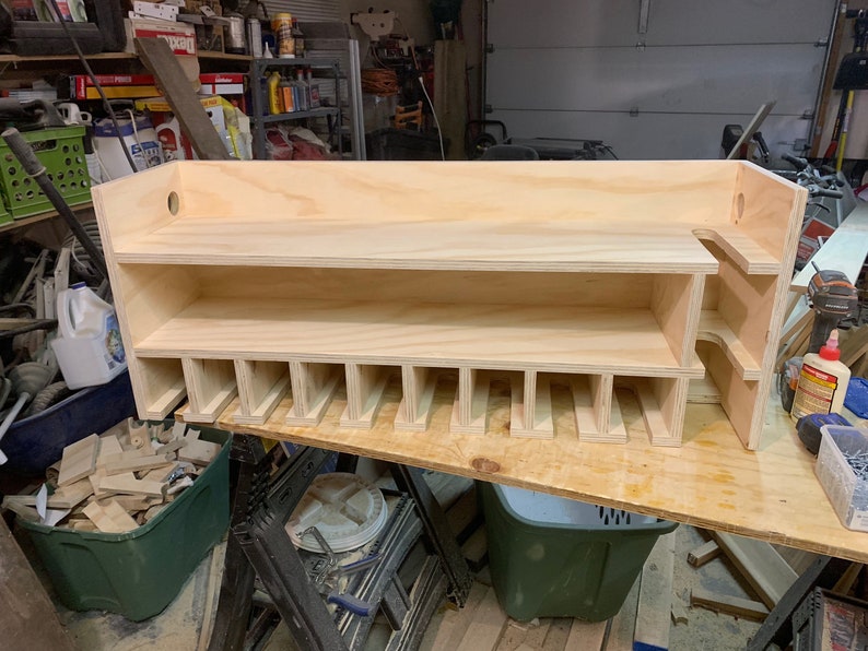 May include: A wooden shelf unit with multiple compartments for storage. The shelf is made of unfinished plywood and has a simple design.