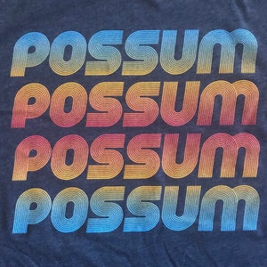 May include: A navy blue t-shirt with the word "possum" repeated four times in a retro, rainbow-colored font.