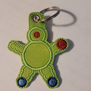 May include: Green felt keychain with a cartoon character design. The character has red and blue details and a silver key ring.
