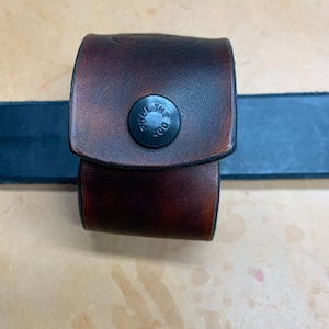 May include: A brown leather belt loop with a black snap button that says "THE DOT PULL".