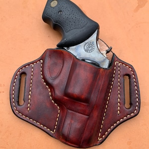 May include: A brown leather holster with a white stitch design. A silver revolver with a black grip is inside the holster.