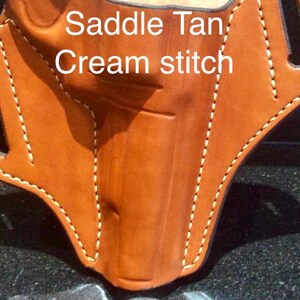 May include: Saddle Tan leather holster with cream stitching. The holster has a cut-out for a gun and a belt loop.