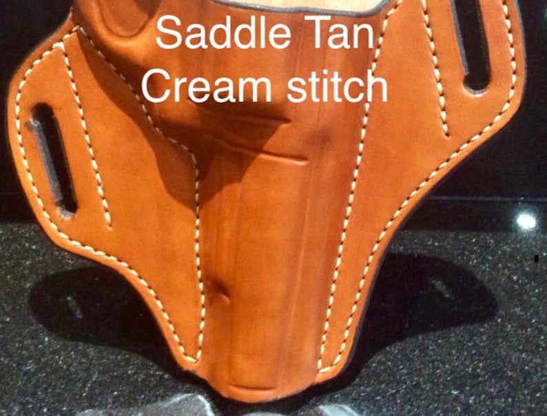 May include: Saddle Tan leather holster with cream stitching. The holster has a cut-out for a gun and a belt loop.