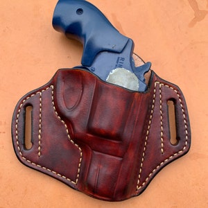 May include: A brown leather holster with a white stitch design. A blue revolver is inside the holster.
