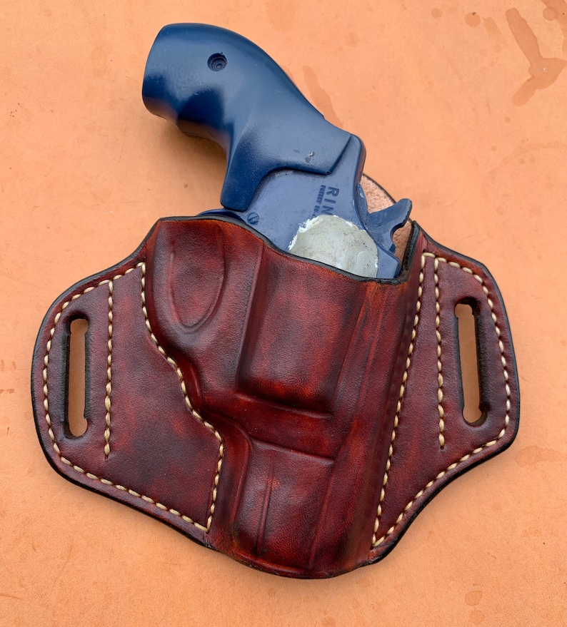May include: A brown leather holster with a white stitch design. A blue revolver is inside the holster.