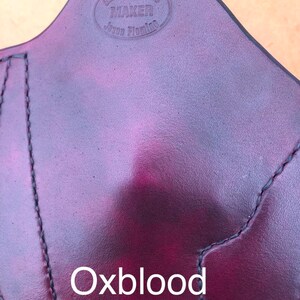 Pu&ograve; includere: Primo piano di una fondina in pelle rosso scuro con il testo "Glock's Holster Maker Jason Fleming" inciso in un cerchio. Il testo "Oxblood" &egrave; stampato sotto la fondina.