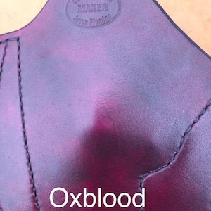 May include: A close-up of a dark red leather holster with the text "Glock's Holster Maker Jason Fleming" embossed in a circle. The text "Oxblood" is printed below the holster.