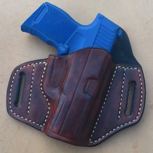 May include: A brown leather holster with white stitching for a blue SIG SAUER pistol.