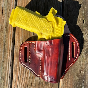May include: A yellow handgun in a brown leather holster. The holster has a stitched design and a belt loop.