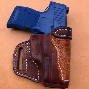 May include: A brown leather holster with white stitching and a blue SIG SAUER pistol inside.