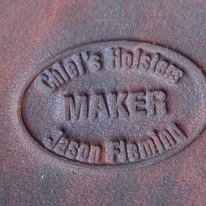 May include: Close-up of a brown leather stamp with the text "Chief's Holsters Maker Jason Flemming" in a circular design.