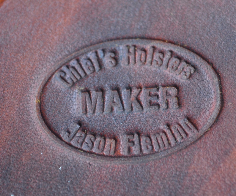 May include: Close-up of a brown leather stamp with the text "Chief's Holsters Maker Jason Flemming" in a circular design.
