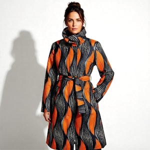 May include: A long coat with a vibrant pattern of orange, black, and white. The coat features a high collar, long sleeves, and a matching belt. The design includes a repeating pattern of orange leaf-like shapes with white dotted accents on a black background. The coat is knee-length.