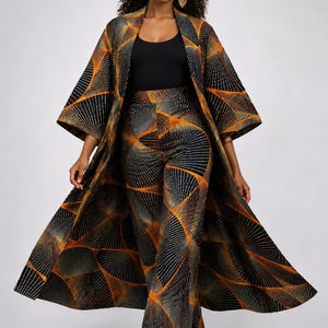 Op de afbeelding: Een driedelig ensemble met een lange, open jas, een bijpassende broek met hoge taille en een zwarte top. De set is voorzien van een geometrisch patroon in zwart, oranje en grijs. De jas valt tot op de enkels.