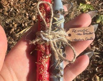 May include: Two intention candles, one red and one gray, are tied together with twine. The red candle is adorned with dried herbs. A small tag reads "Reverse - Hex Breaker Intention Candle."