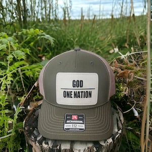 May include: A green and brown trucker hat with a white patch that says "GOD ONE NATION". The hat has a black and red logo that says "Richardson 112" and "Original Trucker Adjustable".