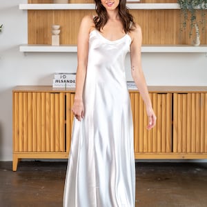 May include: A white satin slip dress with thin straps. The dress is floor-length and has a simple, elegant design.