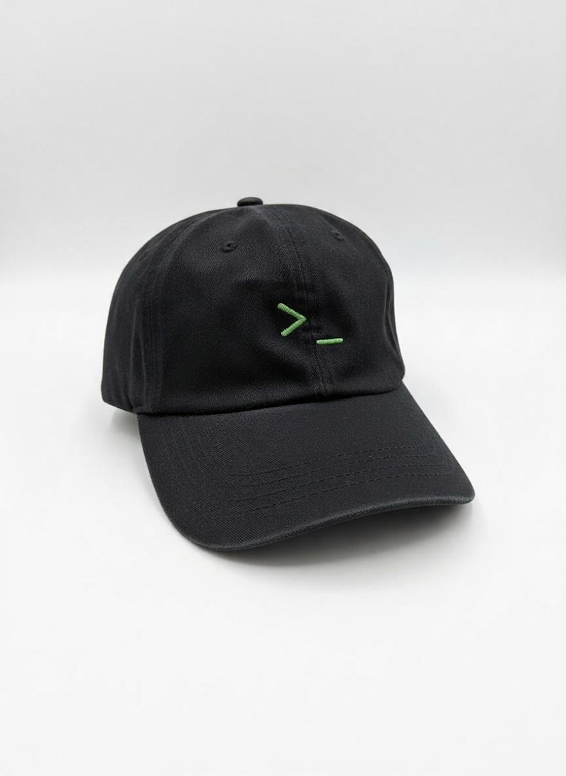 Black baseball cap with embroidered green command line symbol ( >_ ), minimalist tech-inspired design, adjustable strap, unisex casual hat