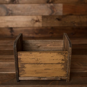K&ouml;nnte beinhalten: Eine rustikale Holzkiste mit einer abgenutzten Oberfl&auml;che. Die Kiste ist leer und hat eine rechteckige Form. Die Kiste ist aus Naturholz gefertigt und hat eine hellbraune Farbe.