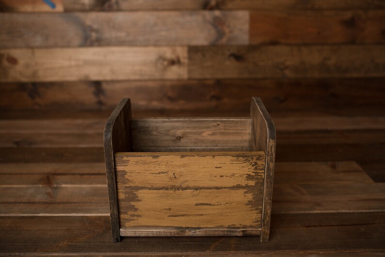 K&ouml;nnte beinhalten: Eine rustikale Holzkiste mit einer abgenutzten Oberfl&auml;che. Die Kiste ist leer und hat eine rechteckige Form. Die Kiste ist aus Naturholz gefertigt und hat eine hellbraune Farbe.