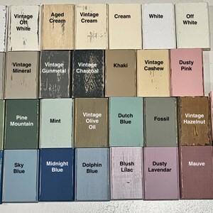 K&ouml;nnte beinhalten: Eine Sammlung von 24 kleinen Holzbl&ouml;cken, die jeweils in einer anderen Farbe lackiert und mit einem Farbnamen beschriftet sind. Die Farben umfassen Vintage-Wei&szlig;, gealterte Creme, Vintage-Creme, Khaki, Vintage-Cashew, staubiges Rosa, Vintage-Moos, Kiefernberg, Minze, Vintage-Oliven&ouml;l, Holl&auml;ndisch Blau, Fossil, Vintage-Haselnuss, Rouge, Ozeanblau, Himmelblau, Mitternachtsblau, Delfinblau, Blush-Lila, staubige Lavendel, Mauve und Vintage-Rosa.