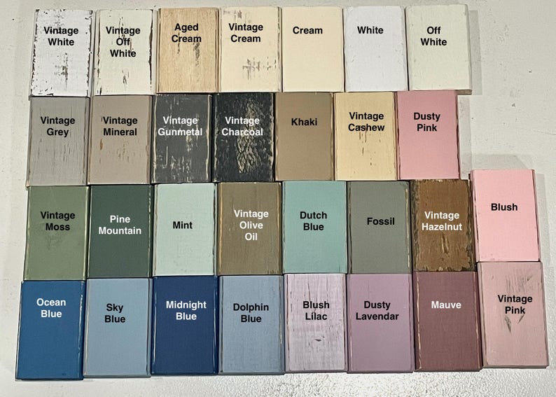 K&ouml;nnte beinhalten: Eine Sammlung von 24 kleinen Holzbl&ouml;cken, die jeweils in einer anderen Farbe lackiert und mit einem Farbnamen beschriftet sind. Die Farben umfassen Vintage-Wei&szlig;, gealterte Creme, Vintage-Creme, Khaki, Vintage-Cashew, staubiges Rosa, Vintage-Moos, Kiefernberg, Minze, Vintage-Oliven&ouml;l, Holl&auml;ndisch Blau, Fossil, Vintage-Haselnuss, Rouge, Ozeanblau, Himmelblau, Mitternachtsblau, Delfinblau, Blush-Lila, staubige Lavendel, Mauve und Vintage-Rosa.