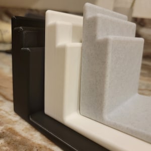 May include: Three 3D printed kitchen organizers in black, white, and speckled gray. The organizers are stacked on top of each other.