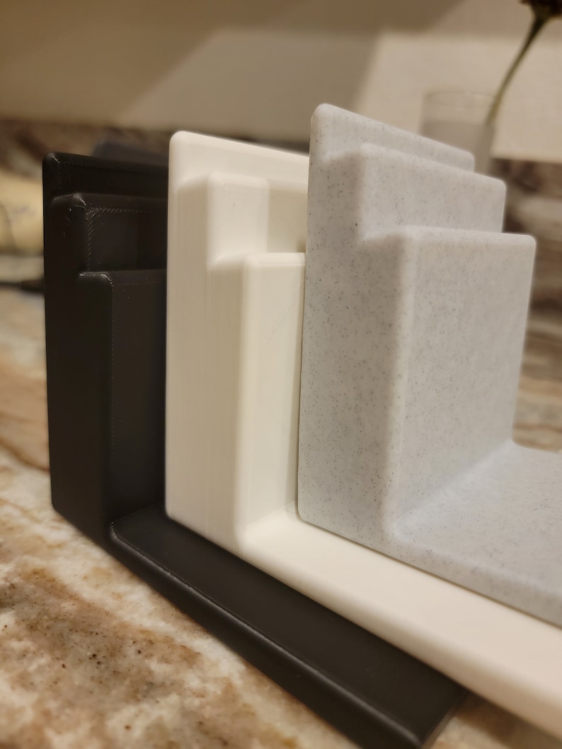 May include: Three 3D printed kitchen organizers in black, white, and speckled gray. The organizers are stacked on top of each other.