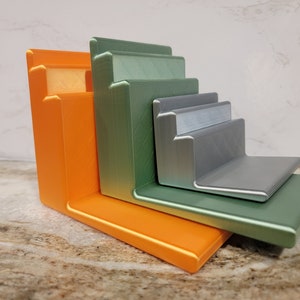 May include: A set of five stacked, angled shelves made of 3D printed plastic. The shelves are in shades of orange, green, and silver.