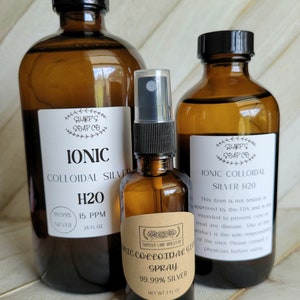 Op de afbeelding: Drie amberkleurige glazen flessen met ionische colloïdale zilveroplossing. De flessen zijn gelabeld met de merknaam "Sharps Soap Co." en de productnaam "Ionic Colloidal Silver H2O". De flessen bevatten respectievelijk 16 fl oz, 16 fl oz en 2 fl oz oplossing. De oplossing is 99,99% zilver.