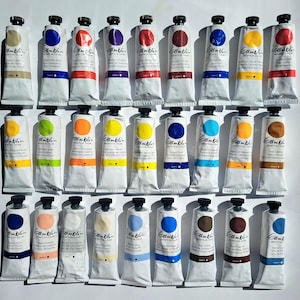 Peut inclure: Une collection de tubes de peinture à l'huile Gamblin Artist's Oil Color, chacun avec un bouchon noir et une étiquette blanche. Les tubes présentent une variété de couleurs, dont des bleus, des rouges, des jaunes et des bruns. Les tubes de peinture sont disposés avec soin.