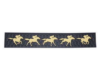 Op de afbeelding: Een zwarte bar mat met een herhaald patroon van gouden racepaarden en jockeys. De mat is rechthoekig en heeft een getextureerd oppervlak. De paarden worden in beweging afgebeeld, wat een race suggereert.