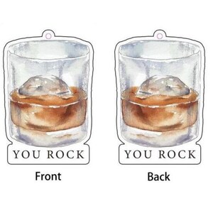 May include: A white, round, hanging tag with a watercolor illustration of a glass of whiskey with an ice cube. The text "You Rock" is printed on the front and back of the tag.