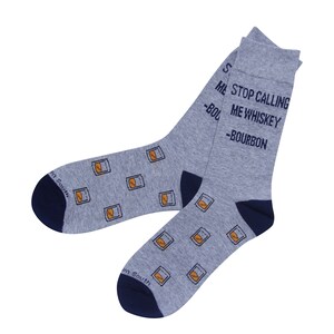 May include: A pair of gray socks with navy blue heels and toes. The socks feature a pattern of orange whiskey glasses and the text "STOP CALLING ME WHISKEY - BOURBON" in navy blue.