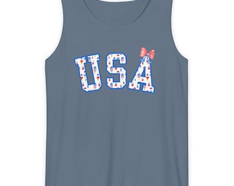 May include: A blue tank top with the word "USA" in white letters filled with red, white, and blue illustrations. A small pink bow is on the right side of the letter "A".
