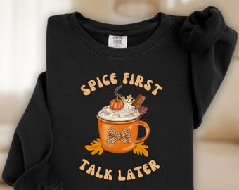 May include: Black sweatshirt with the text "SPICE FIRST TALK LATER" and a graphic of a pumpkin spice latte. The latte has whipped cream, a pumpkin, and a cinnamon stick. The mug has a plaid bow.