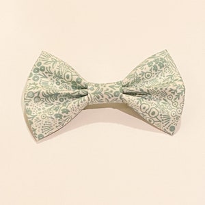 May include: A white bow tie with a green floral pattern.
