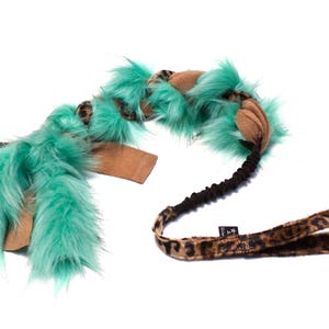 Puede incluir: Un juguete para perro turquesa y marrón con una correa de estampado de leopardo. El juguete está hecho de piel sintética y tiene una banda de goma en el medio.