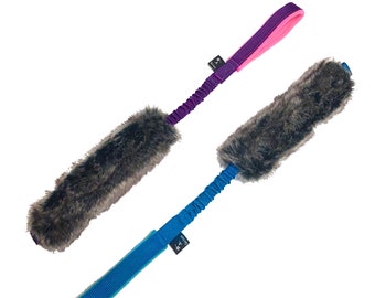 Puede incluir: Dos juguetes para perros con un extremo de piel marrón y un medio elástico extensible. Un juguete tiene un mango morado y rosa, y el otro tiene un mango azul.