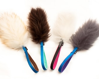 Puede incluir: Cuatro juguetes para perros de peluche con diferentes colores de pelo y asas azules. Los juguetes son blancos, marrones, grises y crema.
