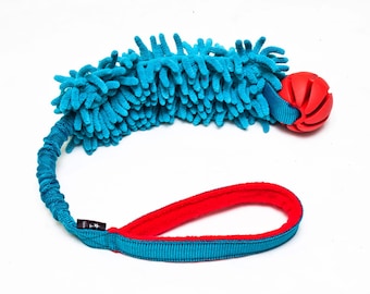 Pode incluir: Um brinquedo para cães azul e vermelho com uma textura felpuda e uma bola de borracha vermelha na ponta.